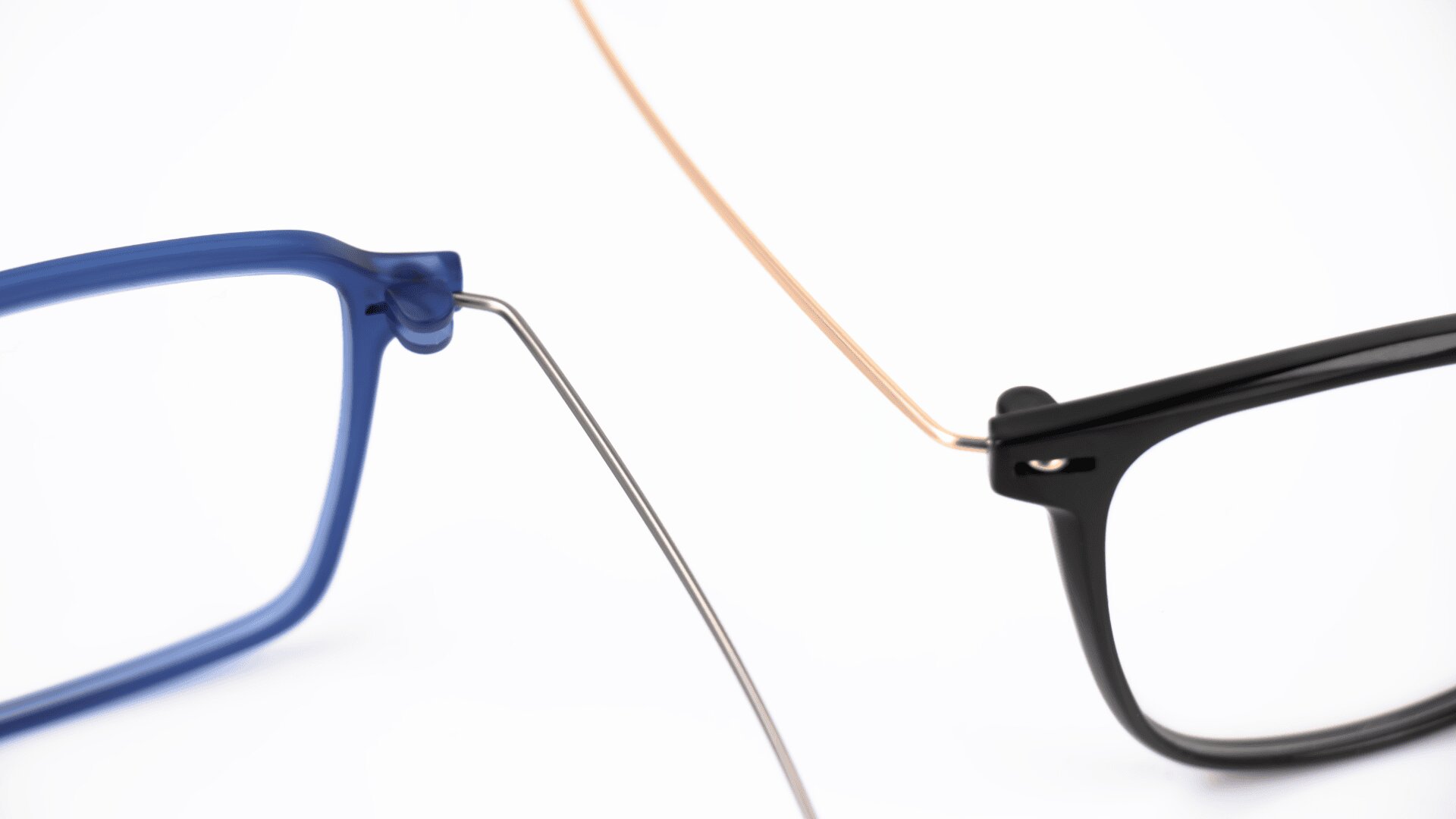 Close-up of two pairs of eyeglasses on a white background: one with a blue frame and silver temple, the other with a black frame and gold temple, positioned so the temples intersect.