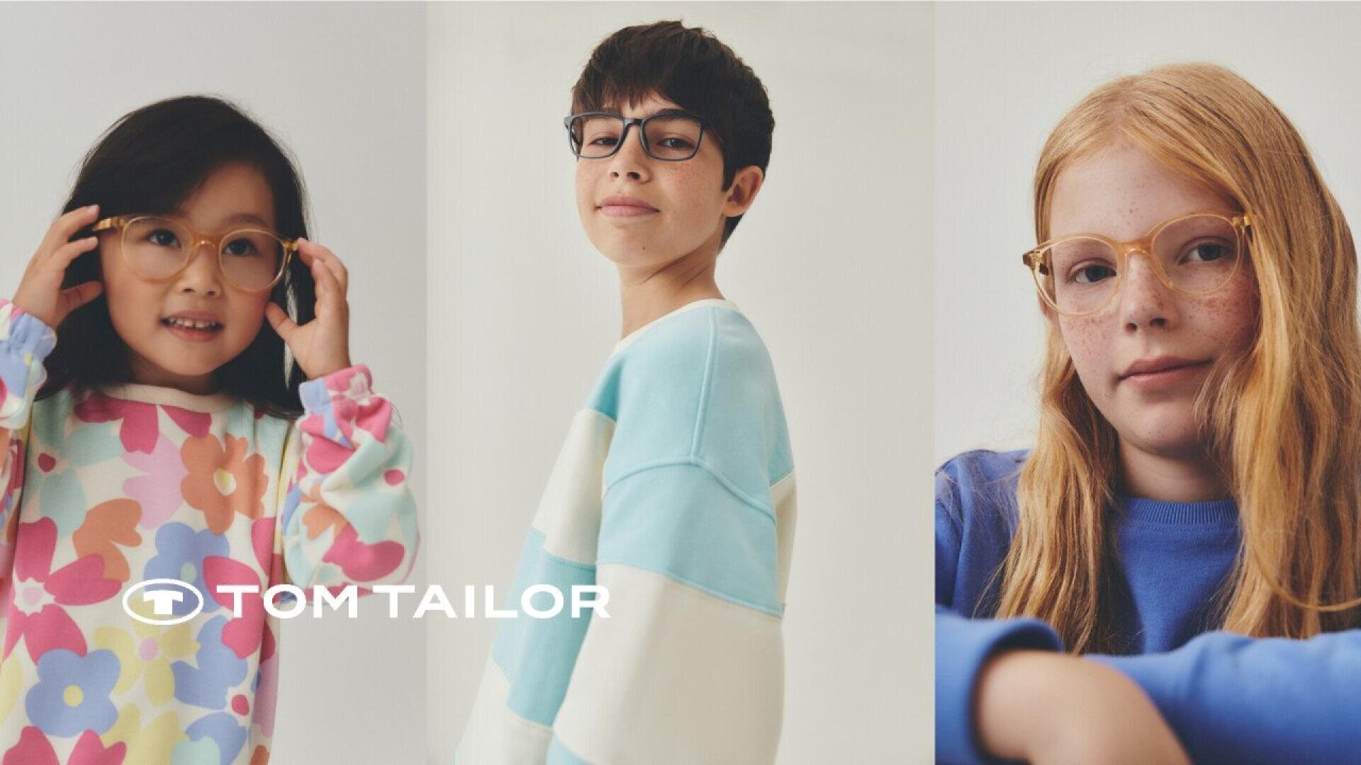 Three children wearing glasses and colorful sweaters pose against a light background. The TOM TAILOR logo is visible in the lower left corner.