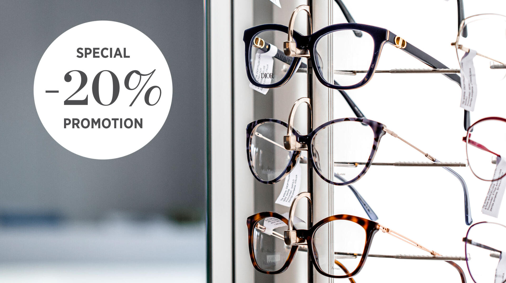 A display of eyeglasses on a rack next to a round sign that reads SPECIAL -20% PROMOTION. The background is softly blurred, highlighting the glasses and the promotional offer.