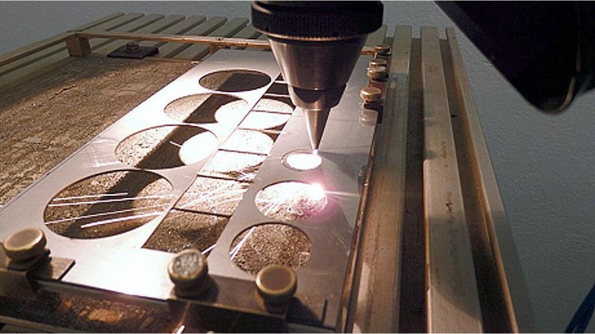 A laser cutting machine precisely cuts circular shapes into a metal sheet, with sparks visible around the laser beam during the process.
