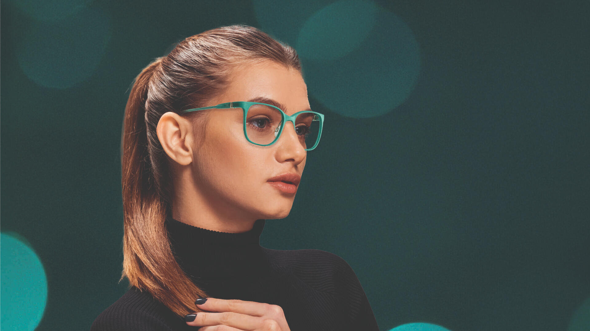 Eine Frau mit glattem braunem Haar zu einem Pferdeschwanz, einer blaugrünen Brille und einem schwarzen Rollkragenpullover posiert vor einem dunkelgrünen Hintergrund mit kreisförmigen Lichteffekten.