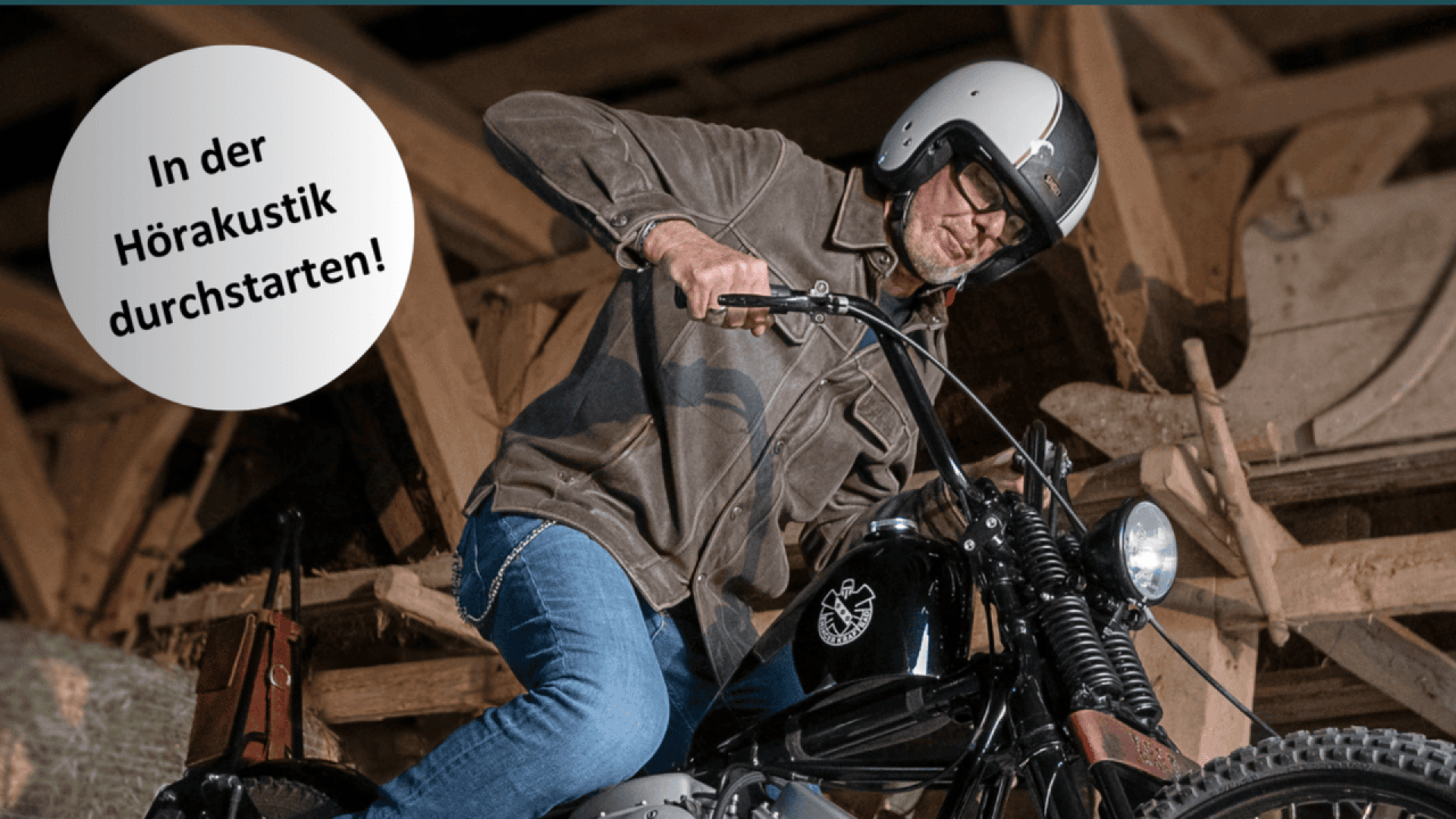 A man wearing a helmet and glasses sits on a vintage motorcycle indoors. A German text bubble reads, In der Hörakustik durchstarten! which means Get started in hearing acoustics! in English.