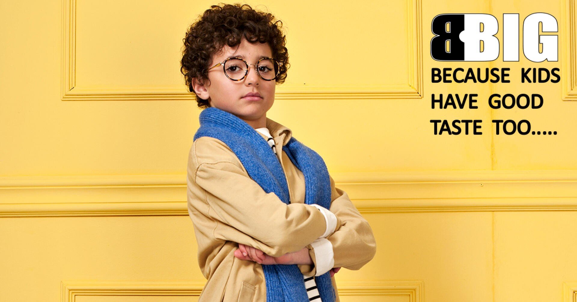 Ein kleiner Junge mit lockigem Haar, Brille und blauem Schal posiert selbstbewusst vor einer gelben Wand. Neben ihm steht: GROSS, weil auch Kinder guten Geschmack haben….