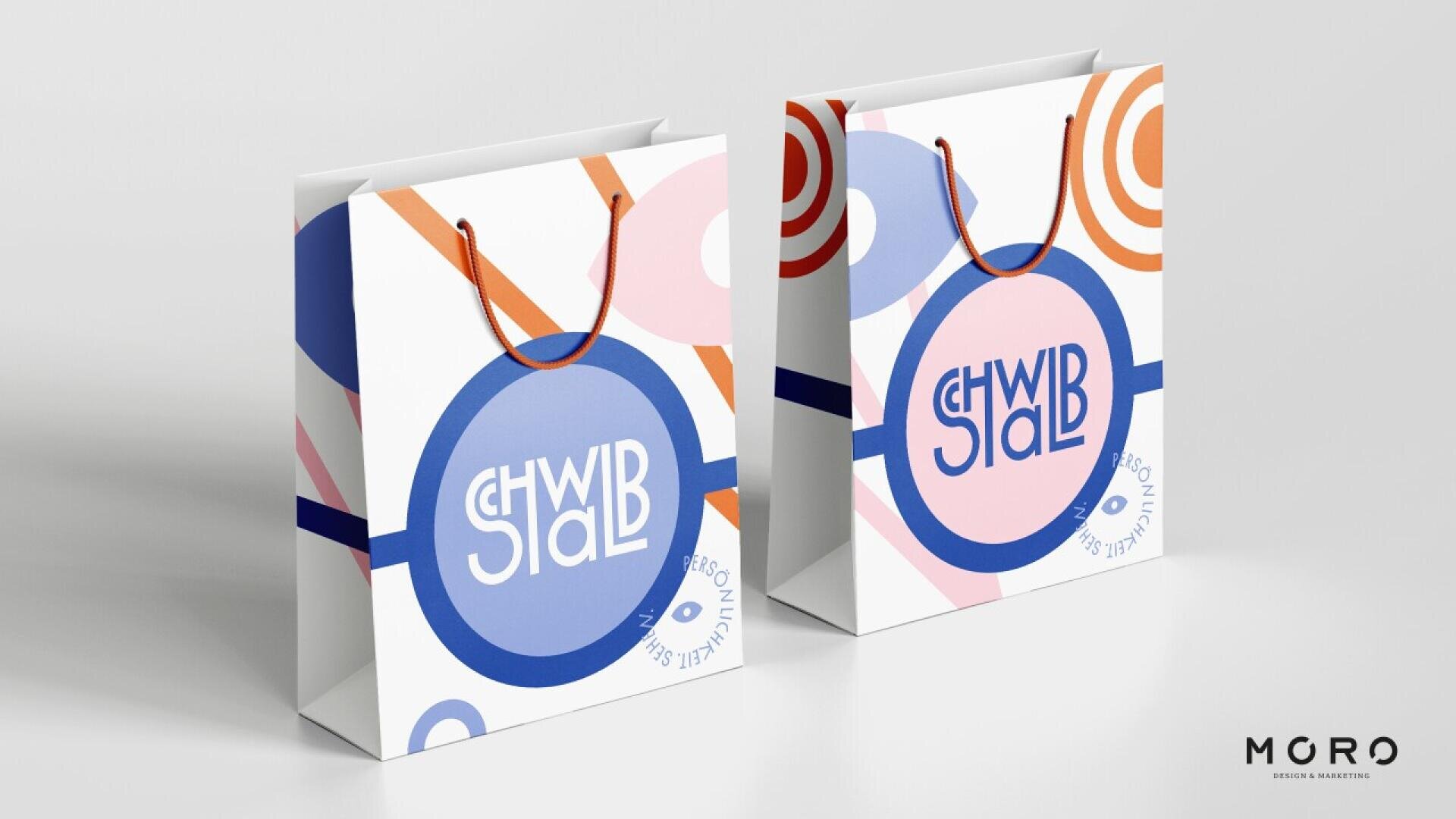 Two colorful shopping bags with abstract orange, blue, and purple geometric designs and round handles are side by side. The logo SHWIB STALB is in a bold, playful font. The bottom right shows the MGRO branding.