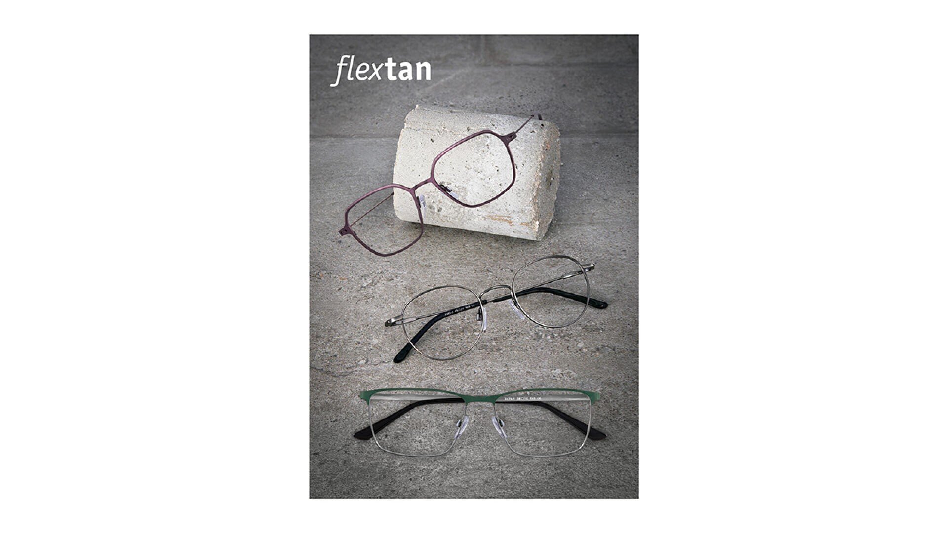 Drei Brillen mit schwarzen Bügeln sind auf einer grauen Steinfläche ausgestellt; eine Brille ruht auf einem Betonblock, während die beiden anderen flach darunter liegen. In der oberen linken Ecke steht das Wort flextan.