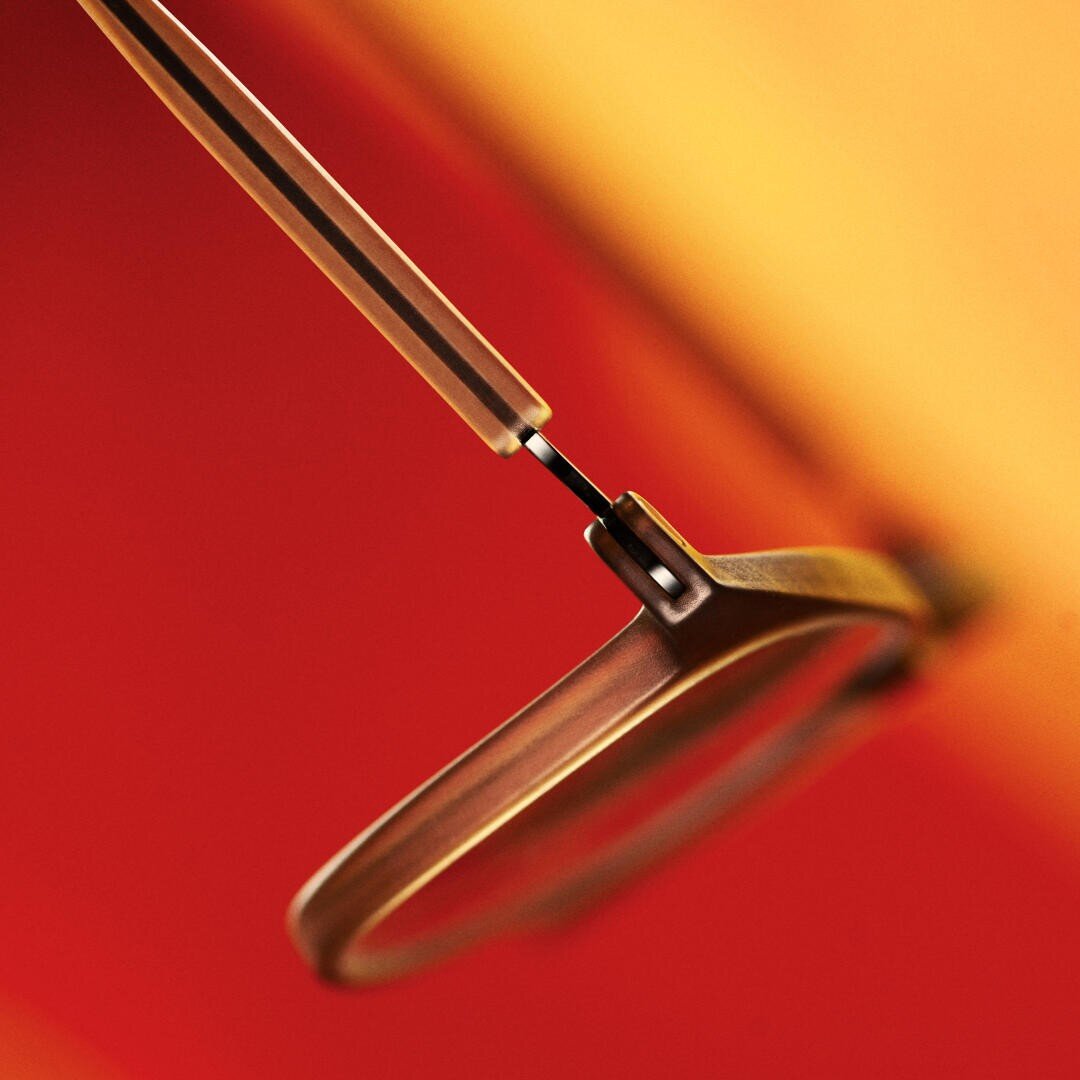 Nahaufnahme einer Brille mit dünnem Metallrahmen vor einem unscharfen Hintergrund mit Farbverlauf in warmen Rot- und Orangetönen. Der Fokus liegt auf dem Scharnier und einem Teil des Glases.