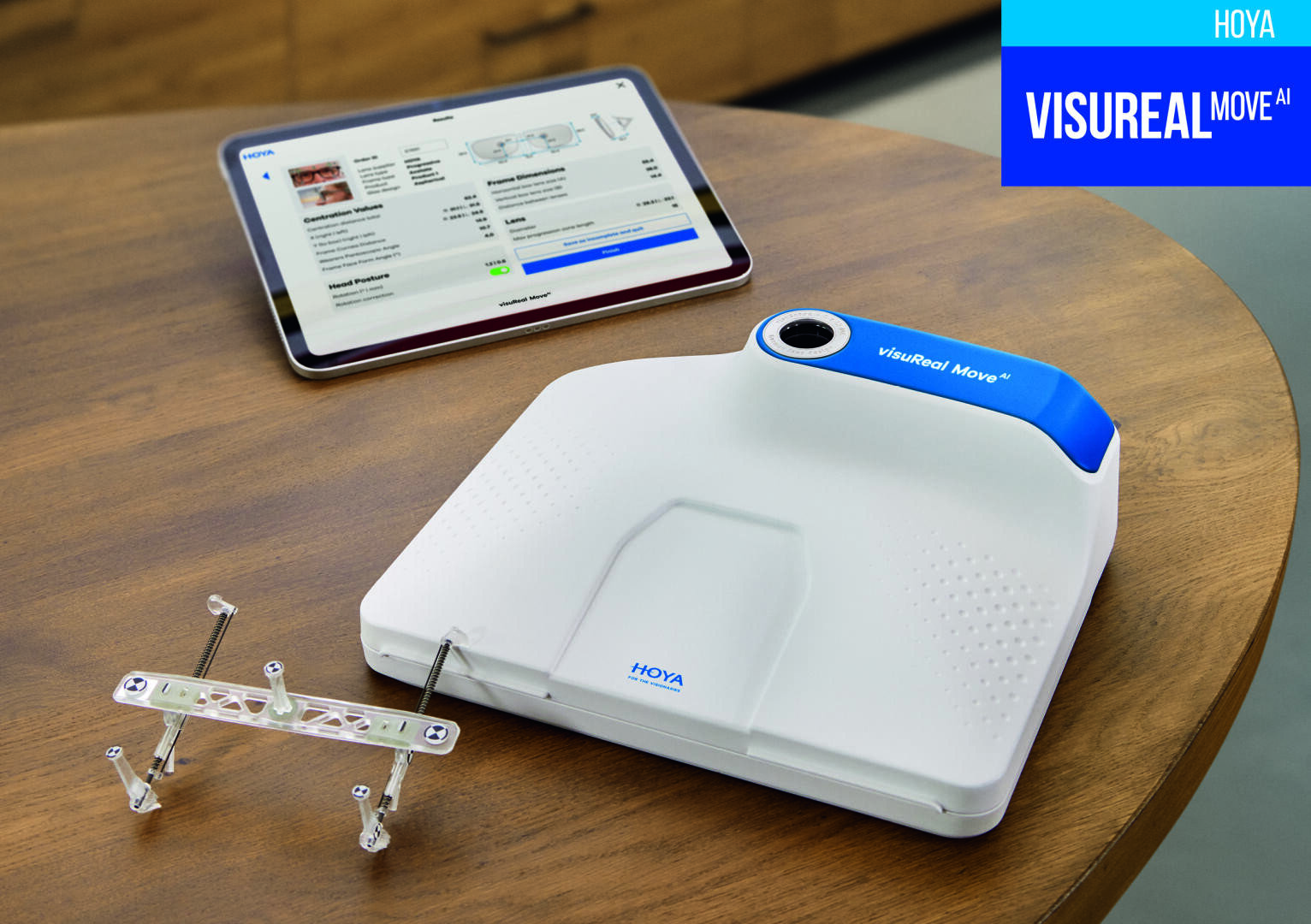 Ein weißes HOYA VISUREAL MOVE AI-Gerät steht auf einem Holztisch neben einem Messgerät und einem Tablet, das Informationen zur Brillenanpassung anzeigt.
