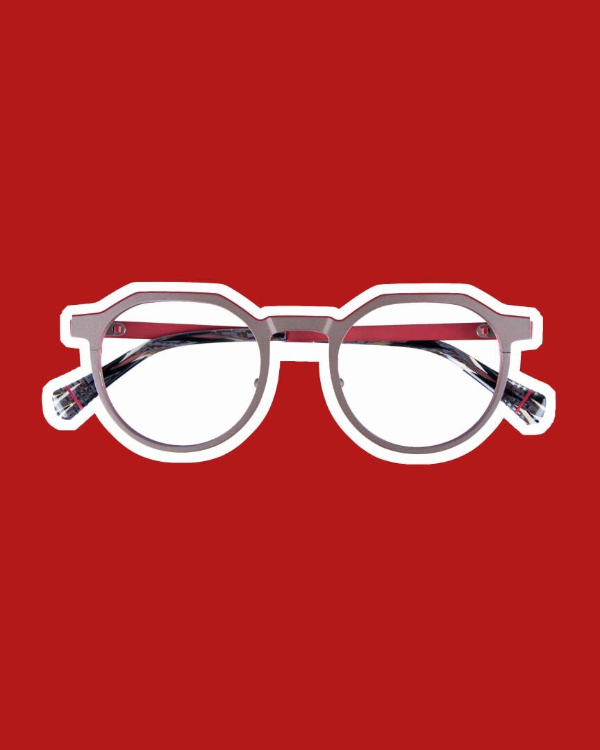 A pair of round glasses with a dark, patterned frame and clear lenses, shown against a plain red background with a white outline around the lenses.