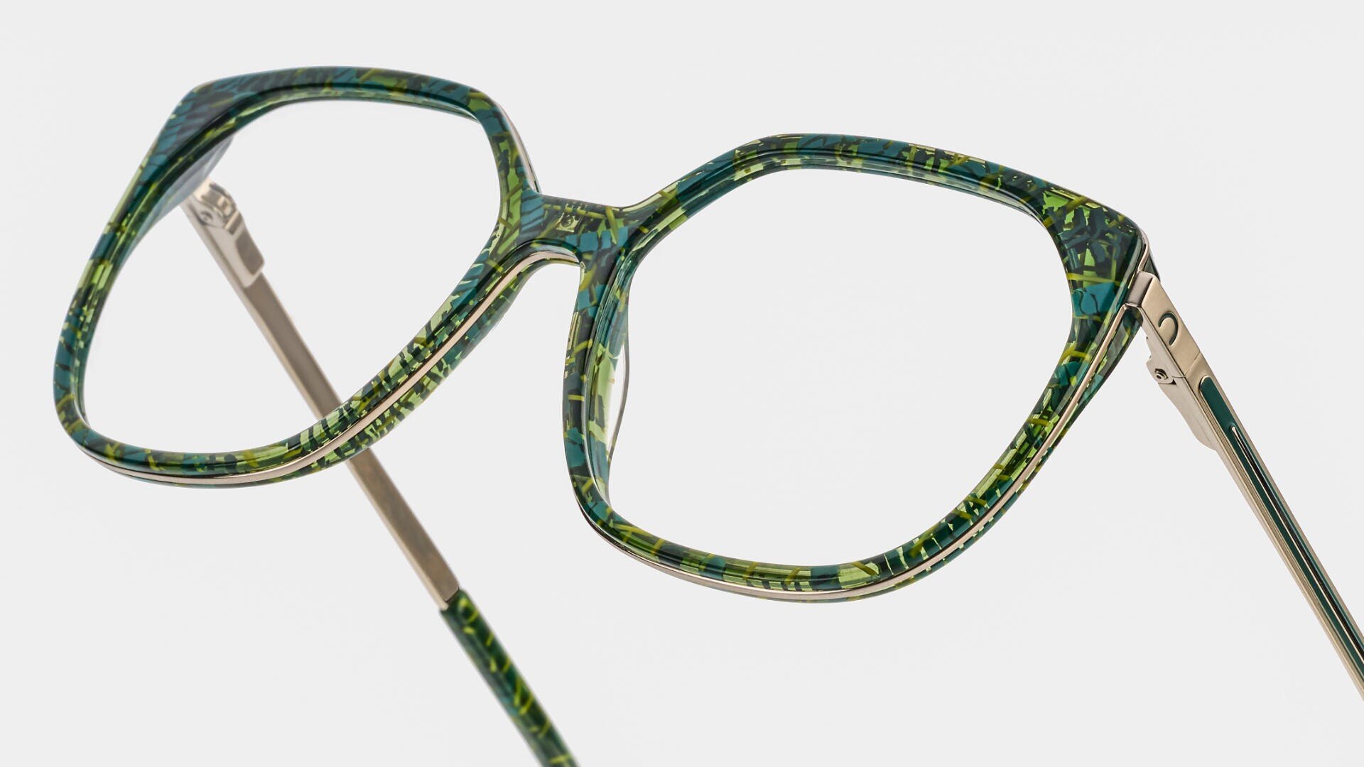 Grün und gelb gemusterte Brille mit großem, geometrischem Rahmen und dünnen Metallbügeln, vor einem schlichten weißen Hintergrund.