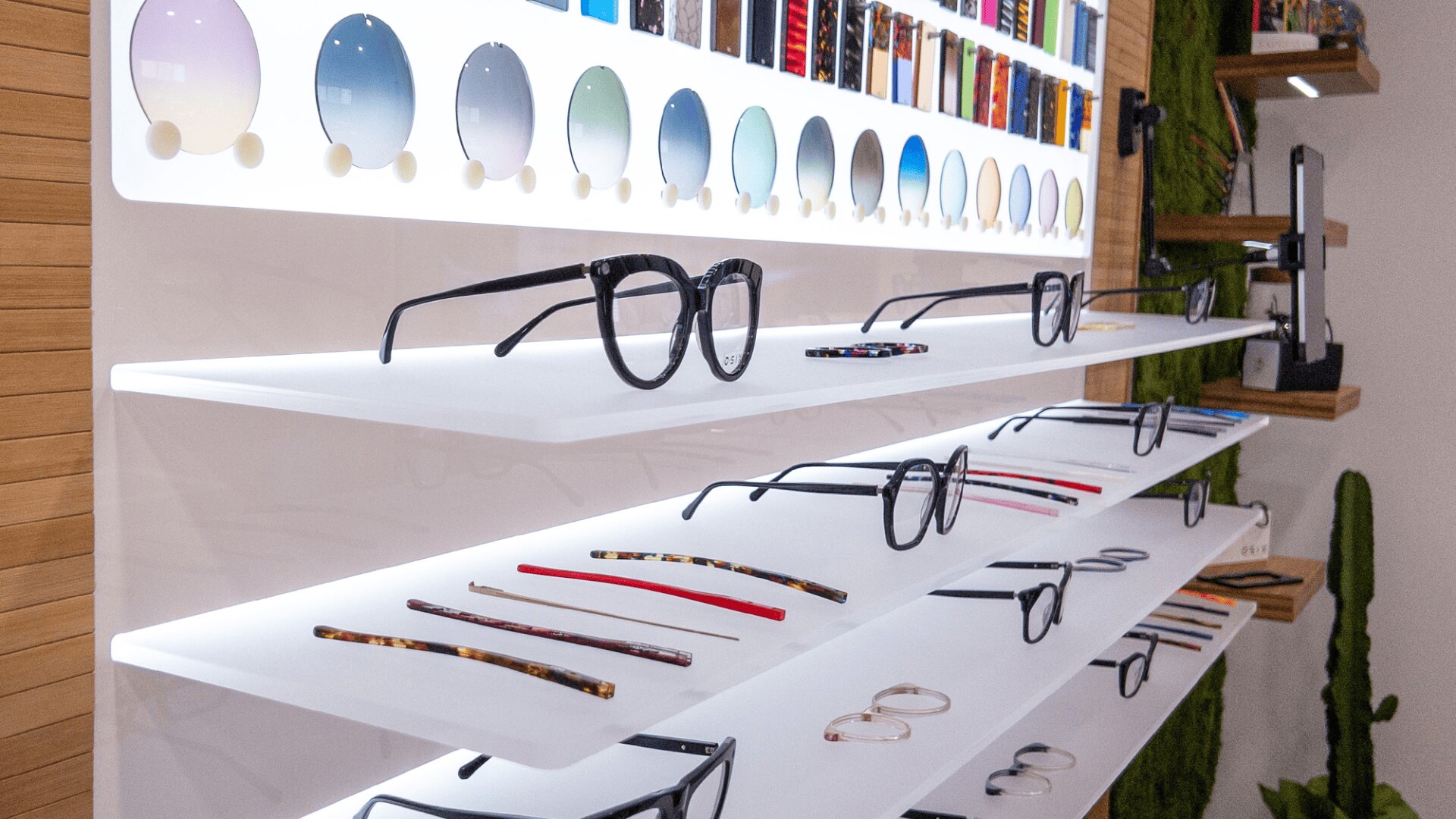 Display shelves with various eyeglass frames and colorful lens samples, neatly arranged in a modern, well-lit eyewear store interior.