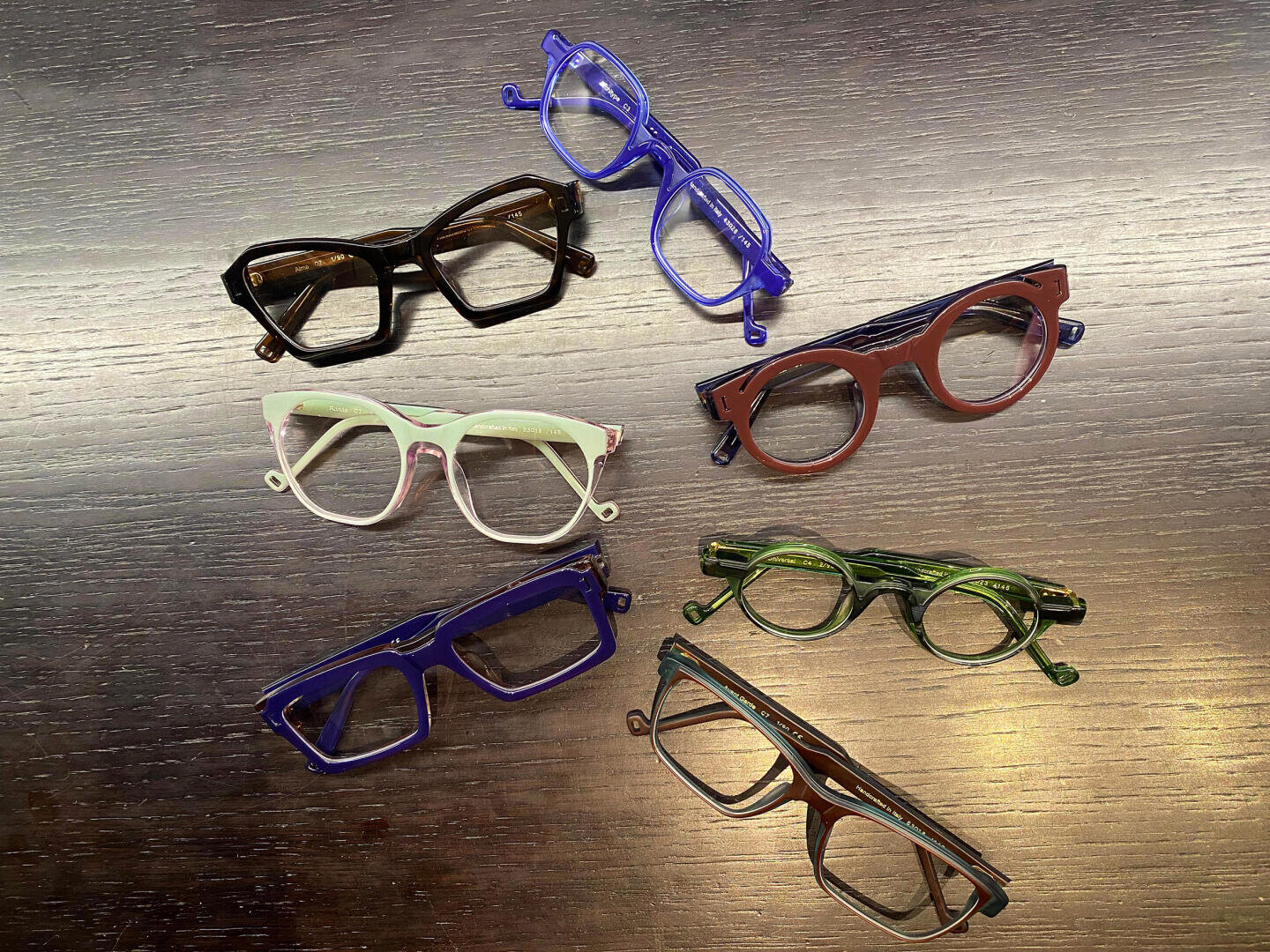 Seven colorful frames with different shapes and designs are arranged on a dark wooden surface. The frames come in different colors, including blue, green, pink, brown and lavender.