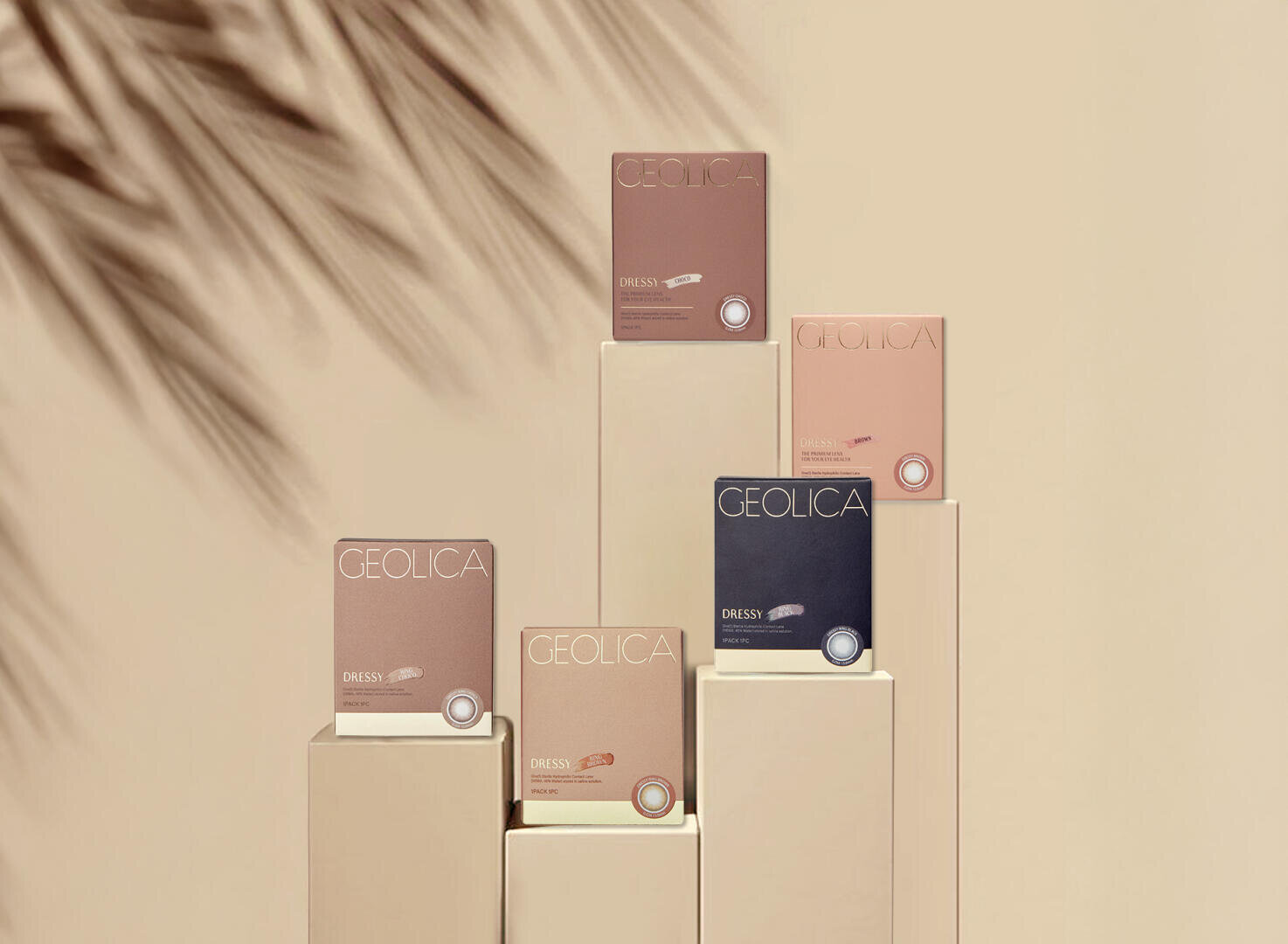 Five boxes of GEOLICA contact lenses in various neutral colors are displayed on beige pedestals, with a palm leaf shadow falling on the left side of the image. The background is in a soft beige tone.