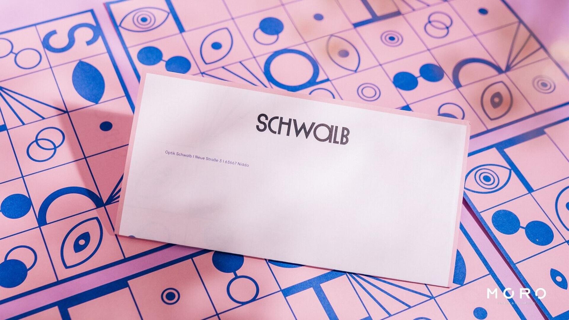 A white envelope labeled SCHWALB rests on a pink and blue patterned surface with geometric and eye designs. The bottom right corner of the image features the word MURO.