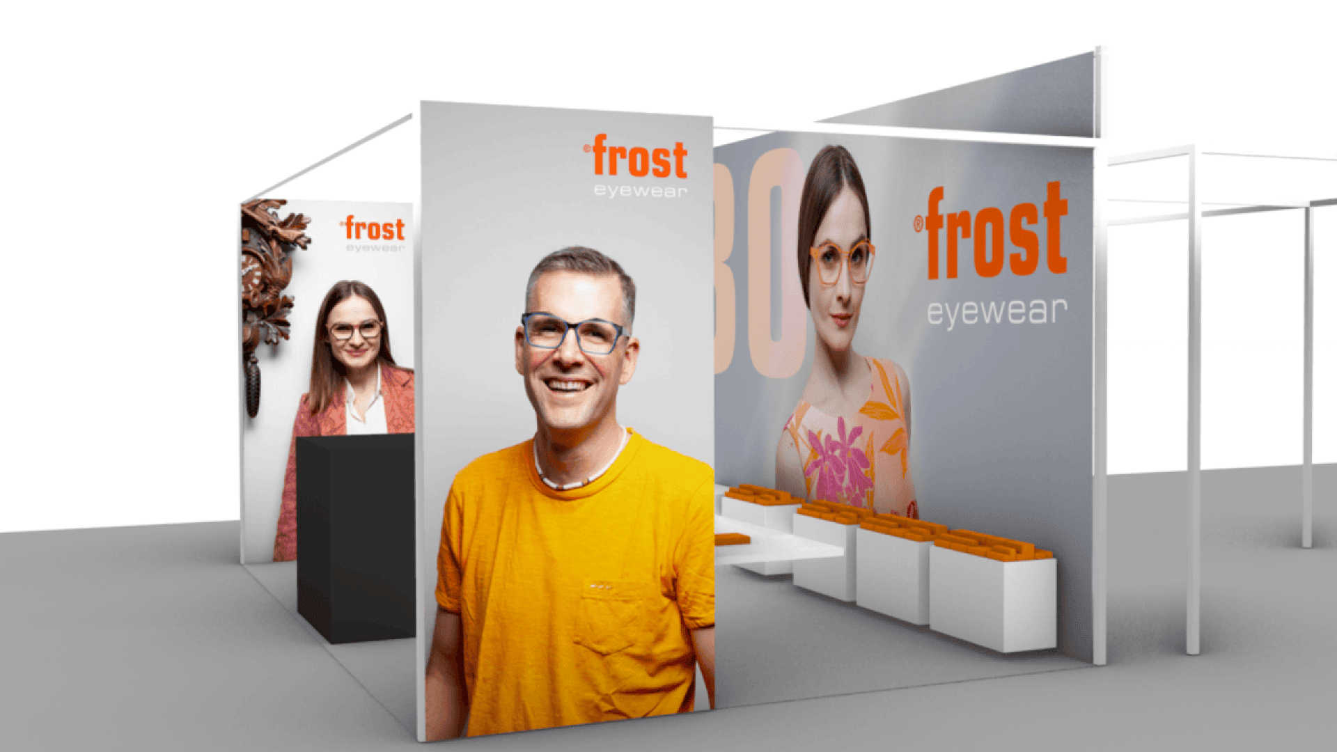 A modern trade show booth for Frost Eyewear features large photos of smiling people wearing glasses, bold frost eyewear branding, and seating with orange cushions against a gray and white backdrop.