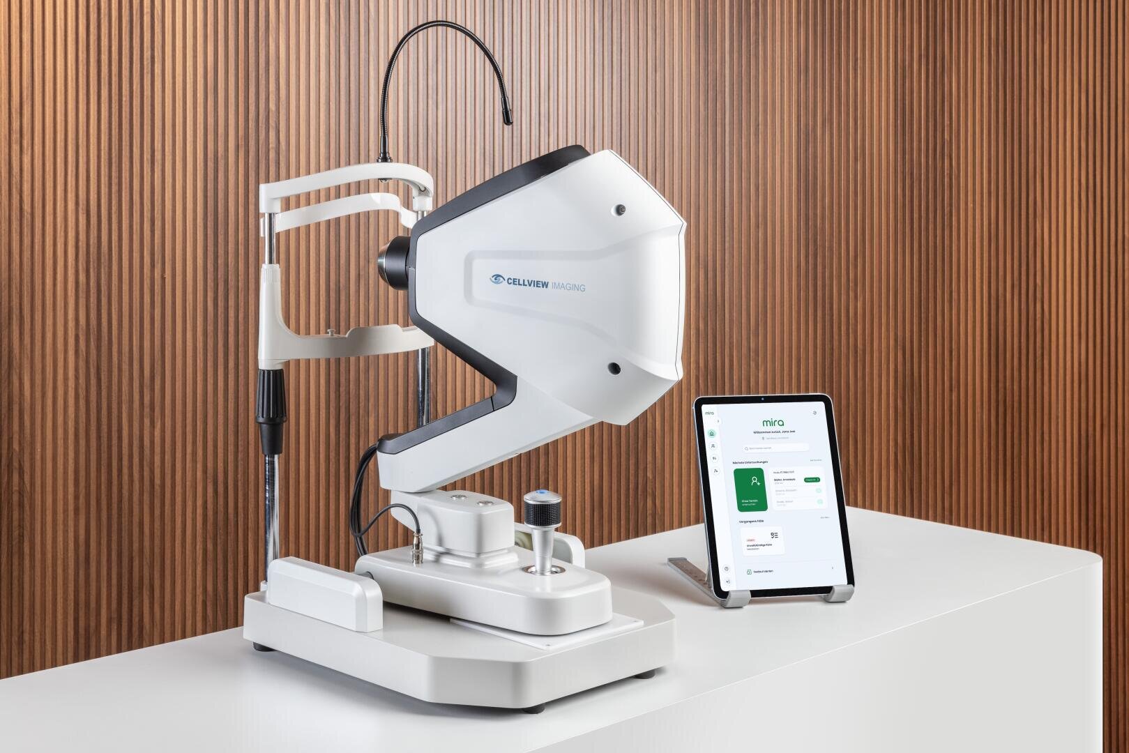 Ein modernes Tischgerät für die Augenuntersuchung steht auf einem weißen Tresen neben einer Tafel mit medizinischen oder diagnostischen Informationen. Der Hintergrund besteht aus einer vertikalen Holzverkleidung.