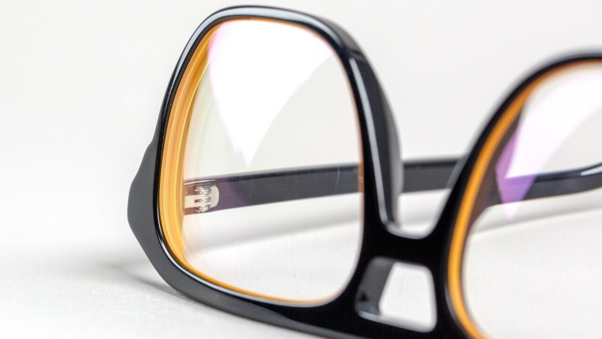Close-up of black eyeglass frames with yellow accents on the inside, highlighting the lenses and stylish frame details against a white background.
