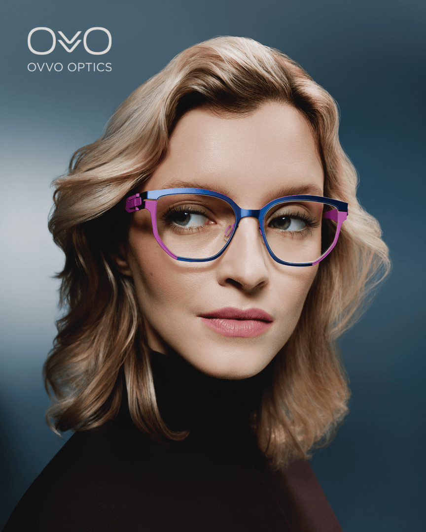 Eine Frau mit gewelltem blondem Haar, die eine große, stilvolle blaue und lila Brille trägt, blickt vor einem blauen Hintergrund mit Farbverlauf zur Seite. Das Logo von OVVO Optics erscheint in der oberen linken Ecke.