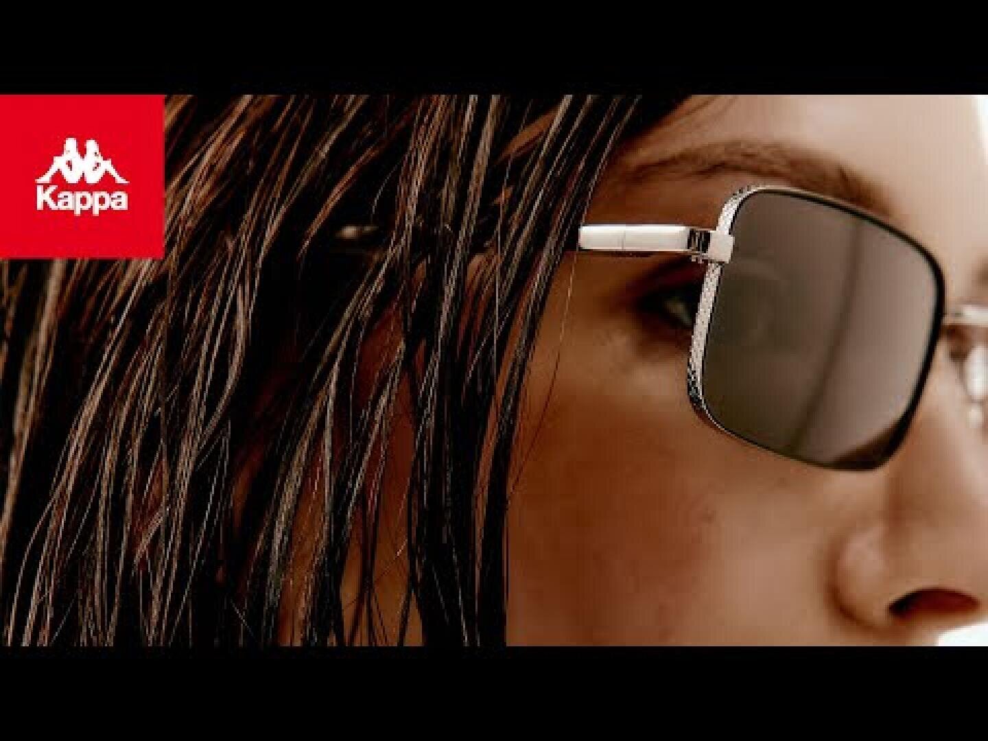 Nahaufnahme einer Person mit nassem Haar und rechteckiger Sonnenbrille. Das Kappa-Logo ist in der oberen linken Ecke auf rotem Hintergrund zu sehen.
