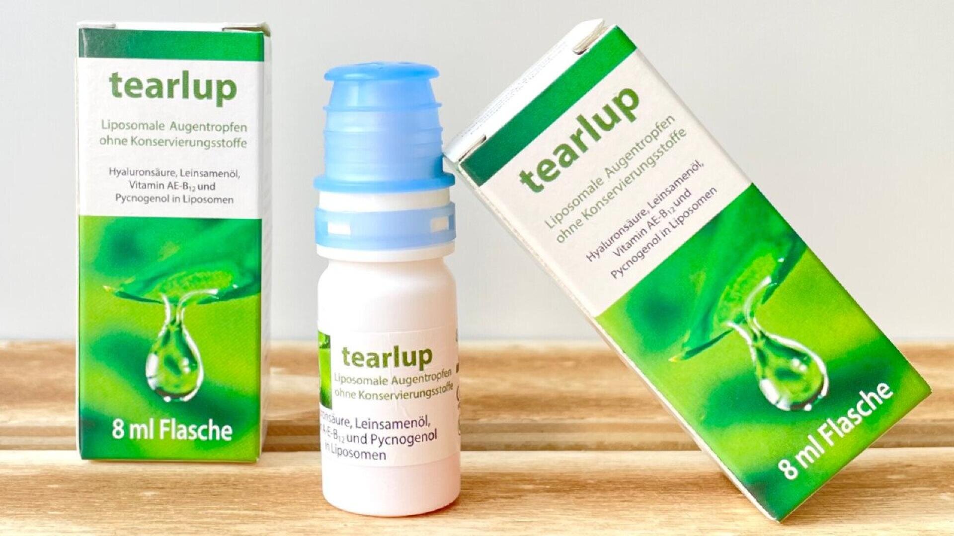 A small white bottle of tearlup eye drops stands between two boxes with green designs, water droplet images, and product details in German. Each box and bottle is labeled 8 ml Flasche.