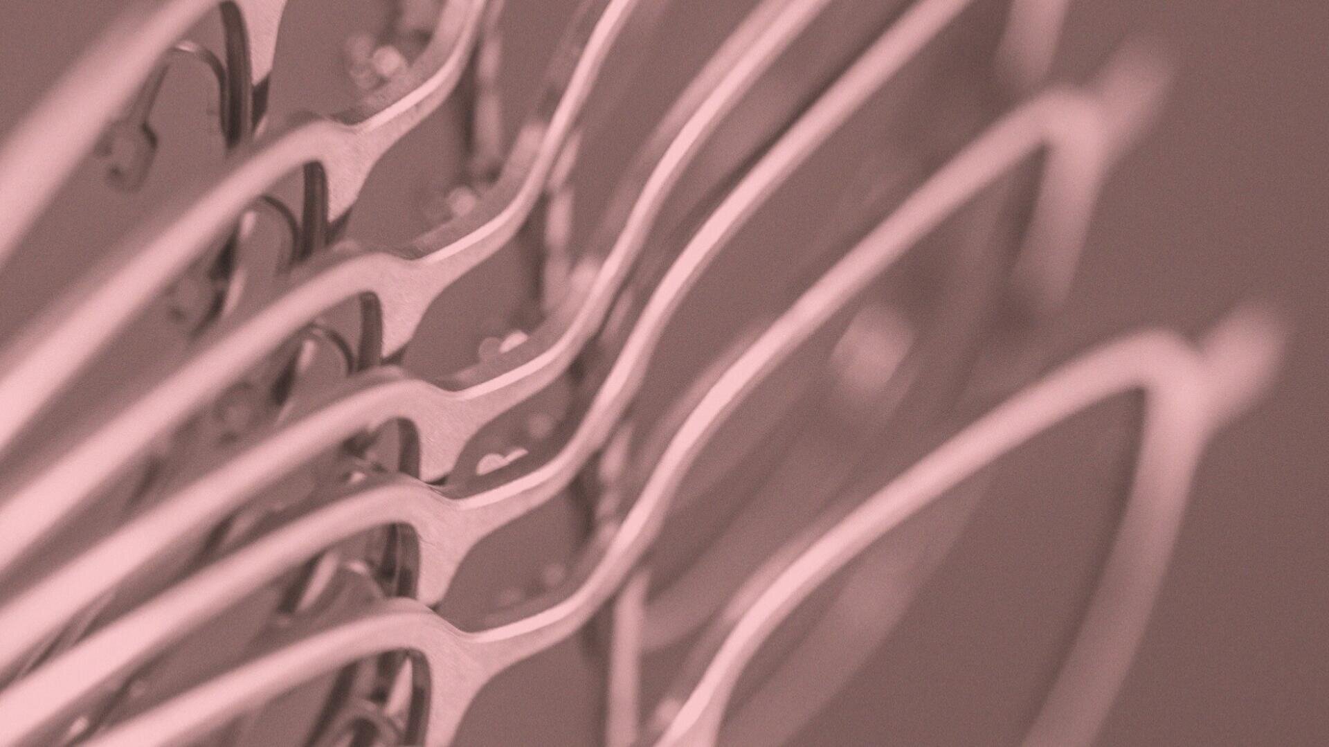 Nahaufnahme von mehreren in einer Reihe angeordneten metallischen Brillengestellen, von der Seite mit geringer Schärfentiefe betrachtet. Das Foto hat einen rosafarbenen Farbton, der ihm ein abstraktes, modernes Aussehen verleiht.