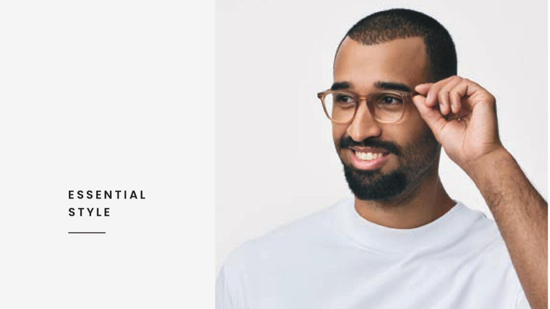 A smiling man with a beard and glasses adjusts his frames while wearing a white t-shirt, next to the text ESSENTIAL STYLE on a plain light background.