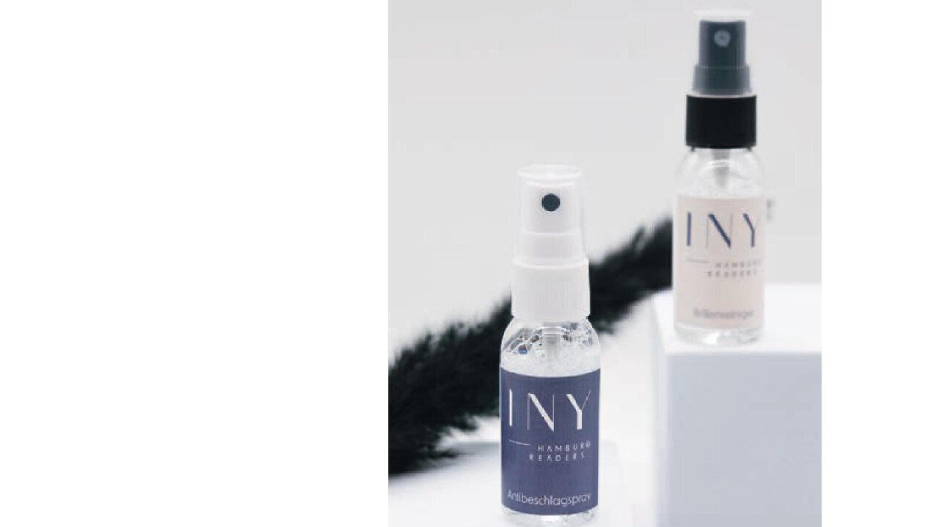Two small spray bottles labeled INY are displayed on a white surface, one in the foreground with a clear cap and one in the background with a black cap. A black feather lies behind them.
