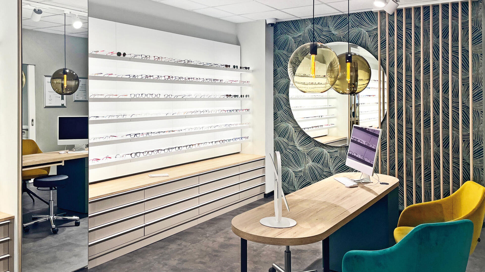 A modern optician’s office with display shelves of eyeglasses, a sleek desk with a computer, yellow and green chairs, patterned wallpaper, and large round mirrors on the wall.