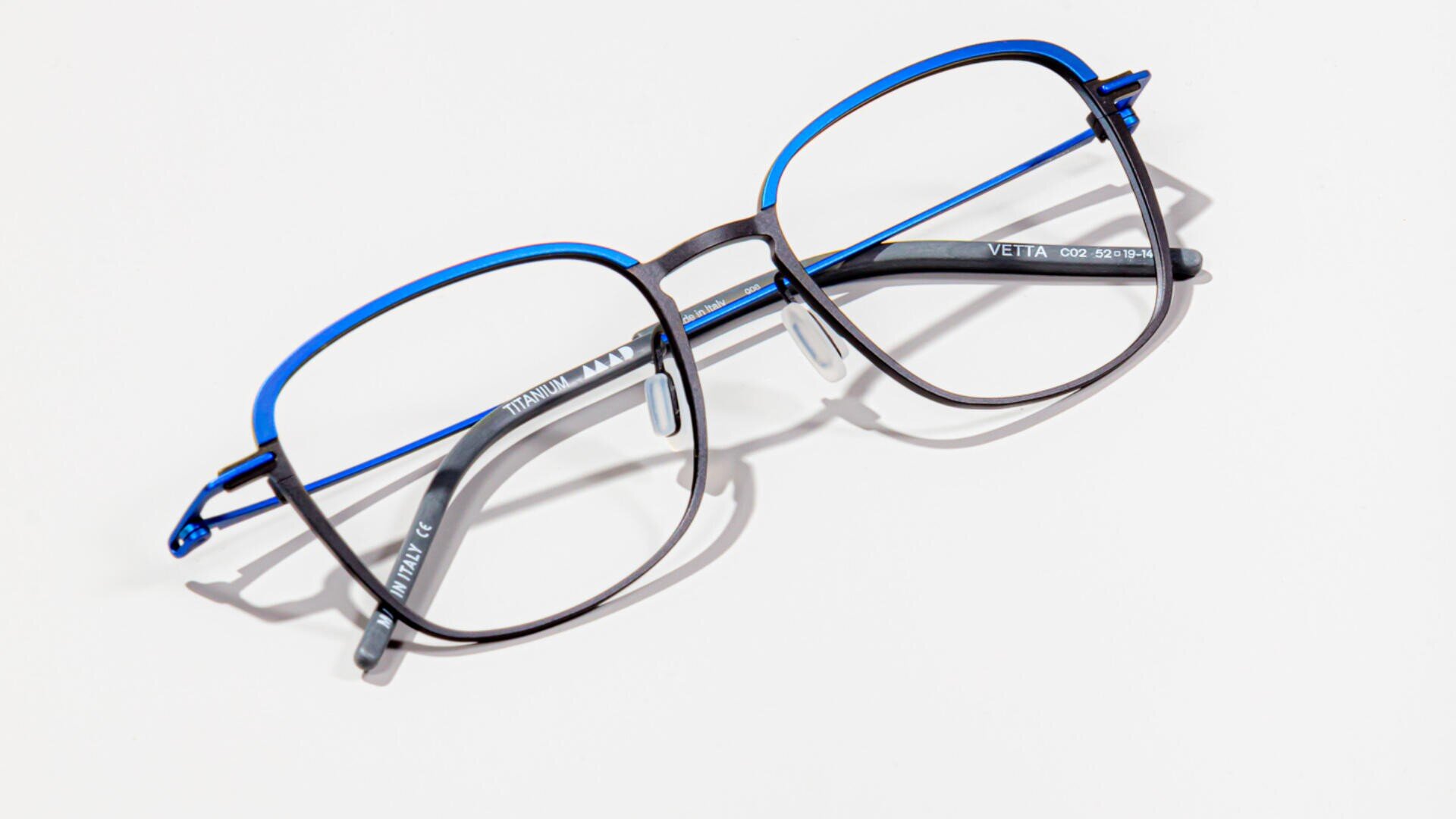 A pair of rectangular eyeglasses with thin black and blue metal frames, resting on a white surface.