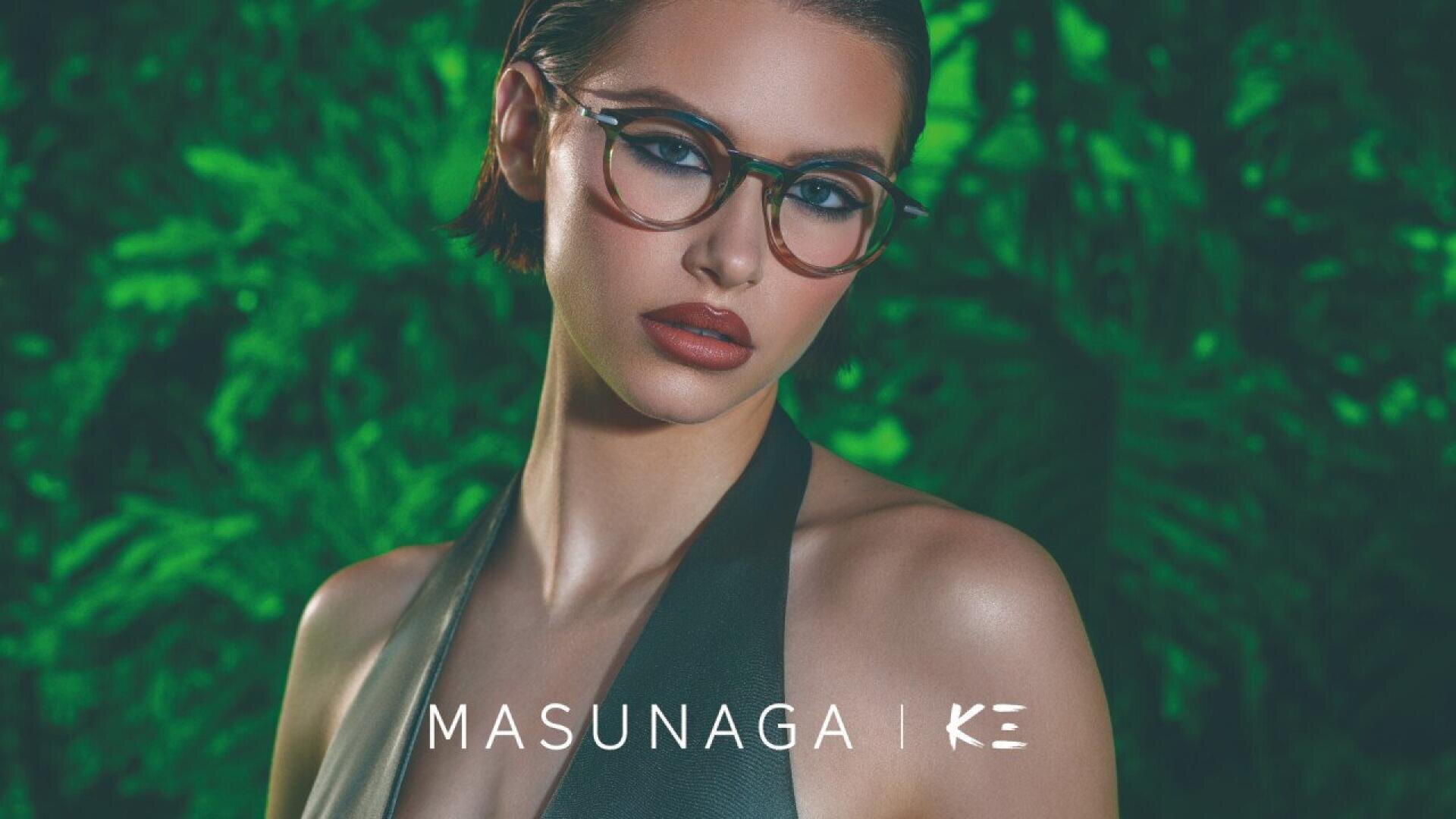 A woman with short dark hair and round eyeglasses poses in front of lush green foliage. She is wearing a sleeveless top and looking confidently at the camera. The text MASUNAGA | KE is displayed at the bottom.