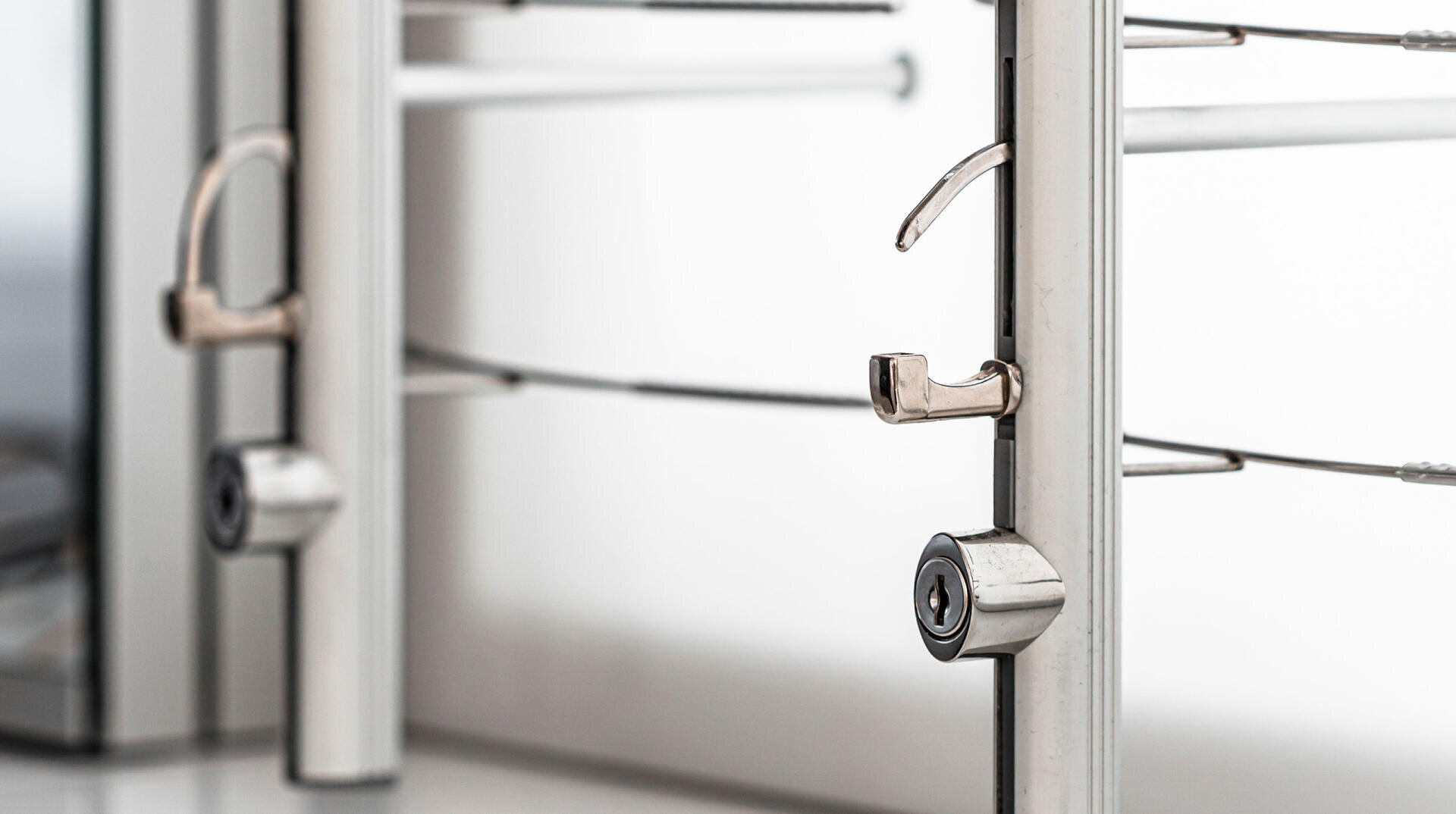 Close-up of two metal locks secured on a stainless steel barrier or gate, with a blurred background and a focus on the locking mechanisms.