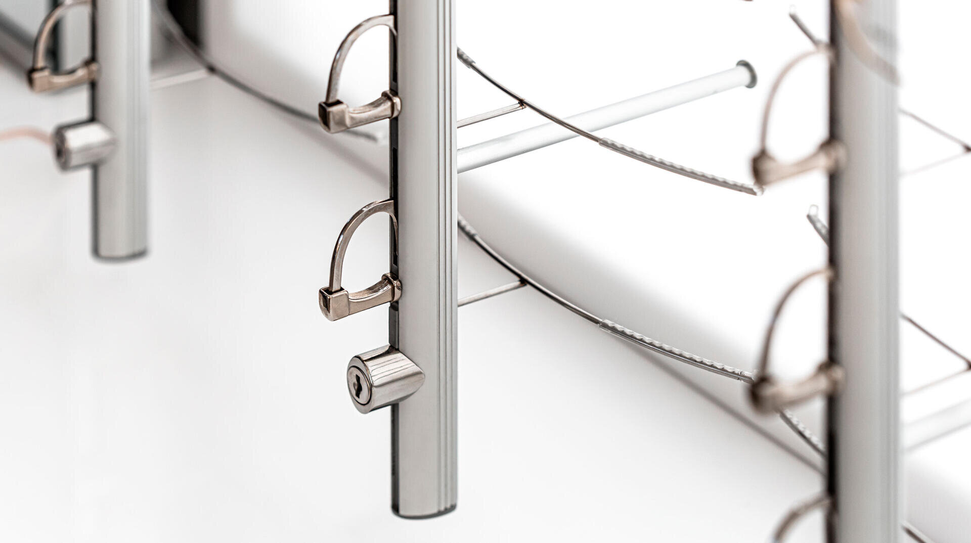 Close-up of metal poles with locks and cables, part of a security or locking system, on a white background. The image emphasizes metallic textures and clean, modern design.