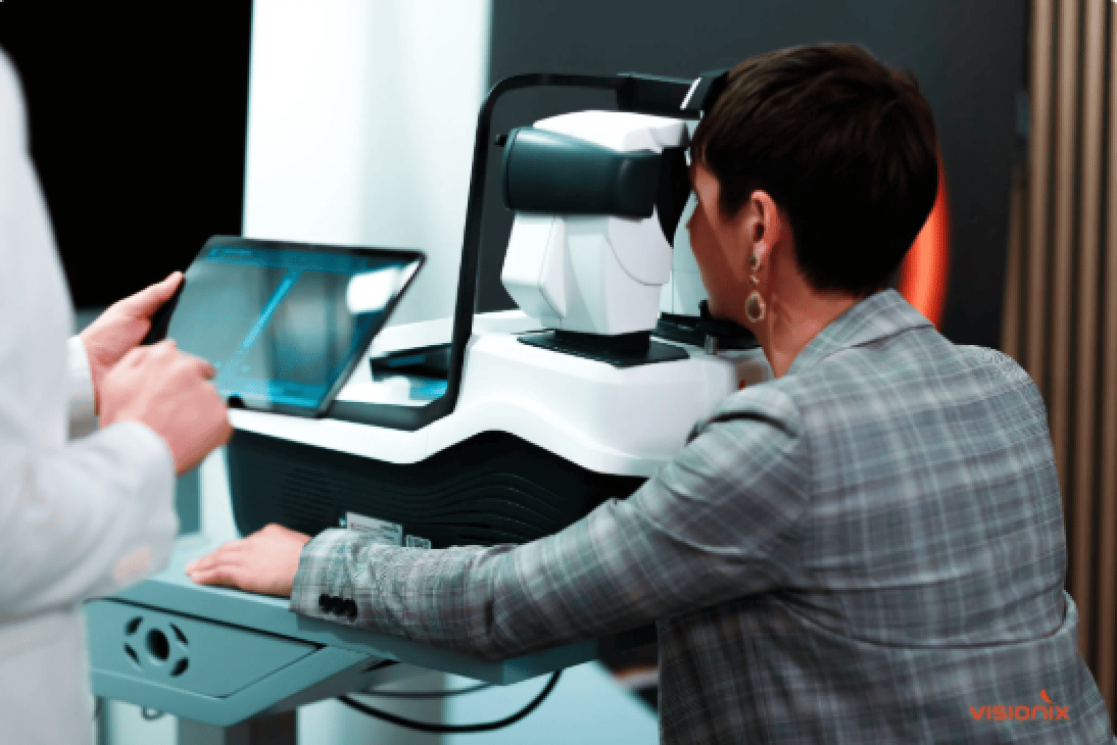 A woman in a checked blazer undergoes an eye examination on a modern eye test device, while a person in a white coat holds a digital tablet.