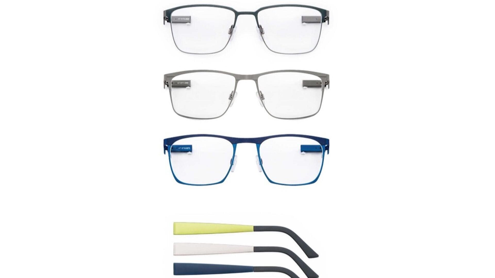Drei Paare rechteckiger Brillen in Schwarz, Silber und Blau sind vertikal gestapelt, darunter zwei Sätze austauschbarer Bügel in Gelb und Marineblau.