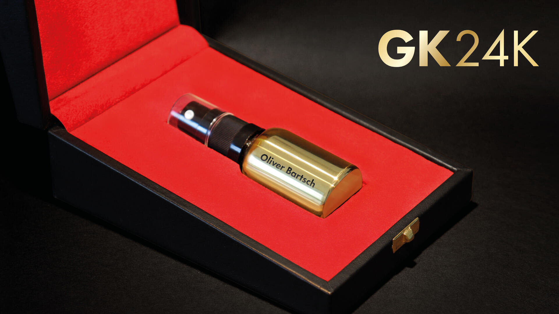 Eine goldene Sprühflasche mit der Aufschrift „Olivier Barsch“ befindet sich in einer schwarzen Schachtel mit rotem Samtfutter. Der Text „GK24K“ erscheint in goldenen Lettern auf der rechten Bildseite.
