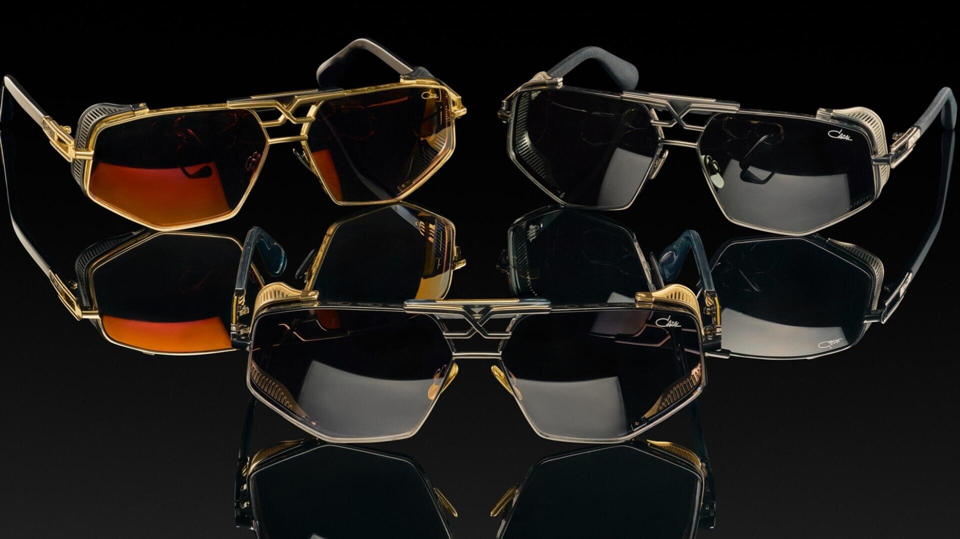 Vier luxuriöse Sonnenbrillen mit goldenen und schwarzen Rahmen sind in einem Halbkreis auf einer reflektierenden schwarzen Oberfläche angeordnet und zeigen getönte und dunkle Gläser mit Farbverlauf.