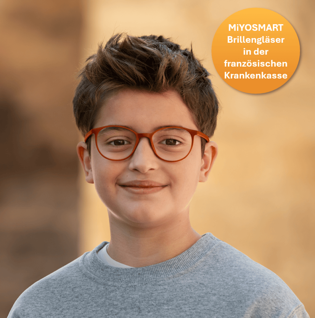 Ein Junge mit kurzen braunen Haaren und roter Brille, der ein graues Sweatshirt trägt, lächelt in die Kamera. In der rechten oberen Ecke steht in einem gelben Kreis: MiYOSMART Brillengläser in der französischen Krankenkasse.