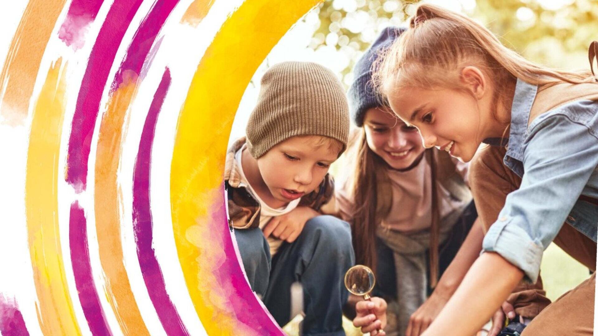 Three young children outdoors examine something on the ground with a magnifying glass. They are smiling and appear curious. Colorful painted arcs in shades of yellow, orange, and pink partially frame the left side of the image.