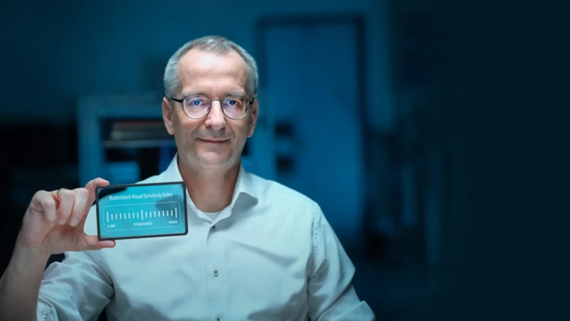 Ein Mann mit Brille und weißem Hemd hält eine transparente Karte hoch, auf der Robust Facial Similarity 2.0 mit einem Ladebalken angezeigt wird. Der Hintergrund ist dunkel und unscharf.