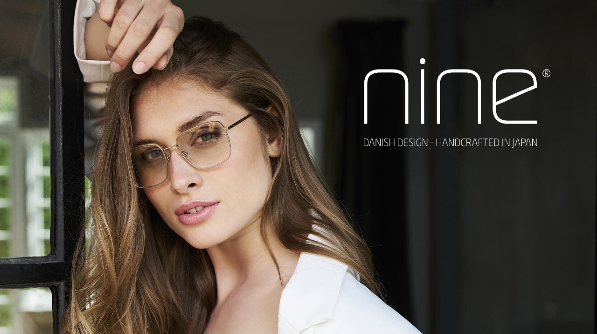 A woman with long brown hair wearing gold-rimmed eyeglasses looks at the camera. Next to her is the logo nine and the text Danish Design - Handcrafted in Japan on a dark background.
