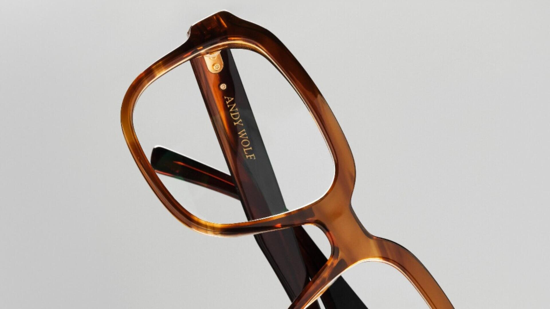 Close-up of brown, rectangular eyeglasses with the brand name ANDY WOLF in gold lettering on the inside of the arm, set against a plain light background.