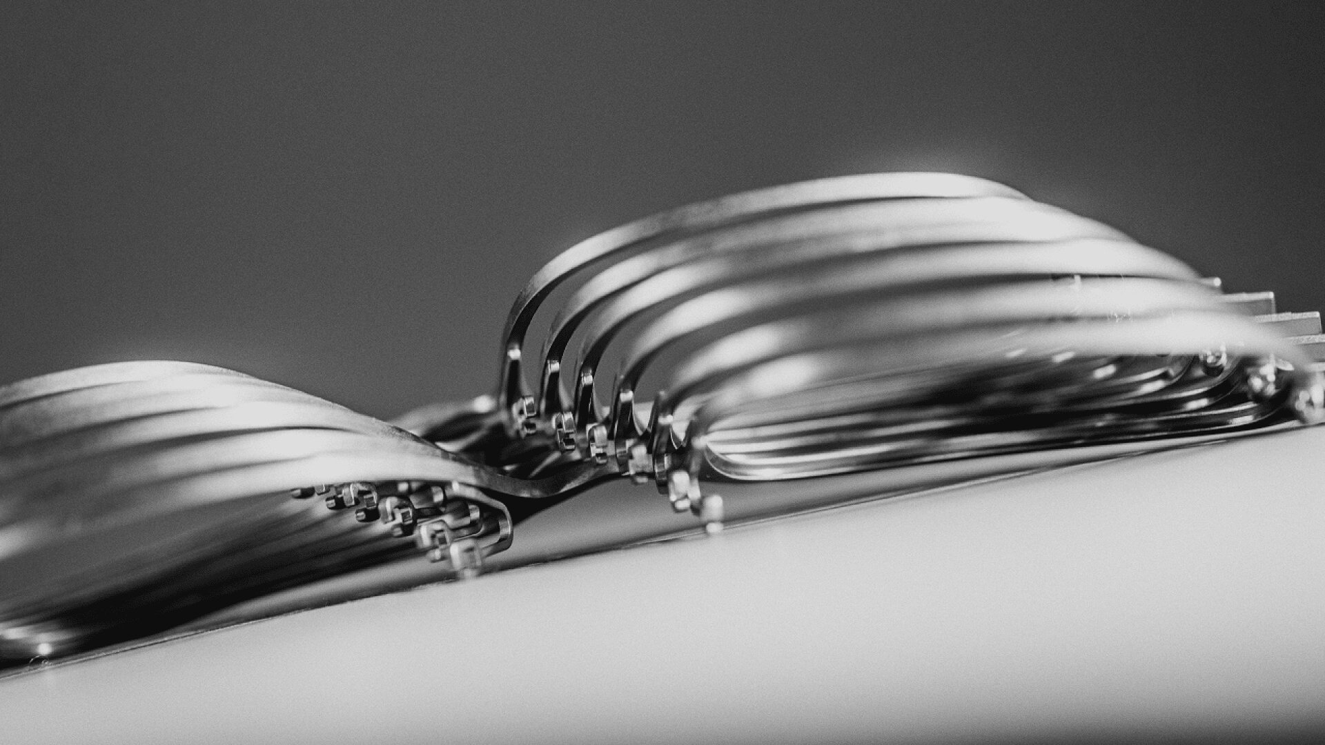 A close-up, black and white image of several metal forks stacked together, showing their curved tines and handles in a layered, abstract arrangement.