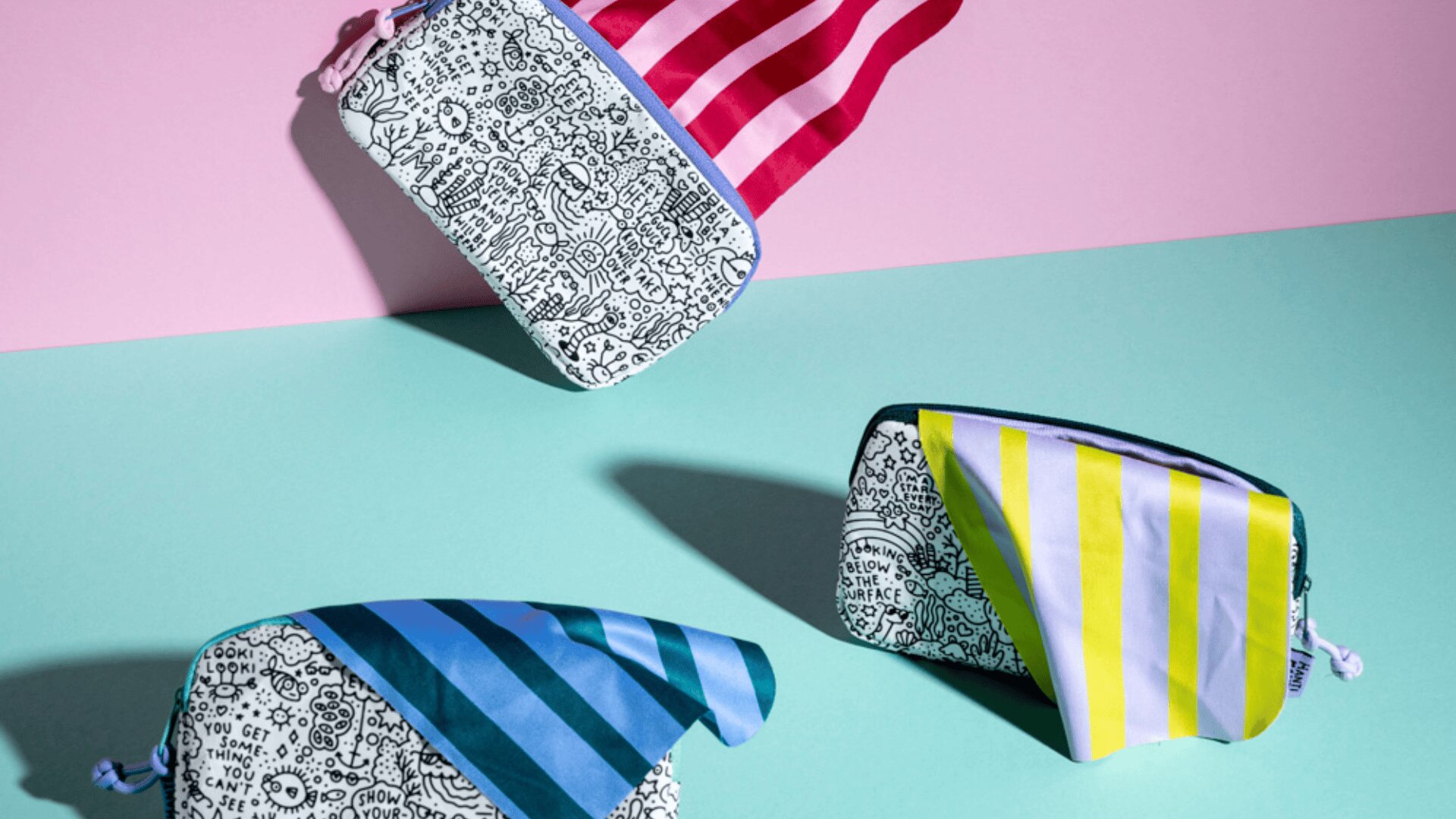 Drei gemusterte Taschen mit schwarz-weißen Kritzeleien und bunten Streifen (rot, blau und gelb) sind auf einem zweifarbigen, pastellfarbenen Hintergrund in Pink und Teal angeordnet.