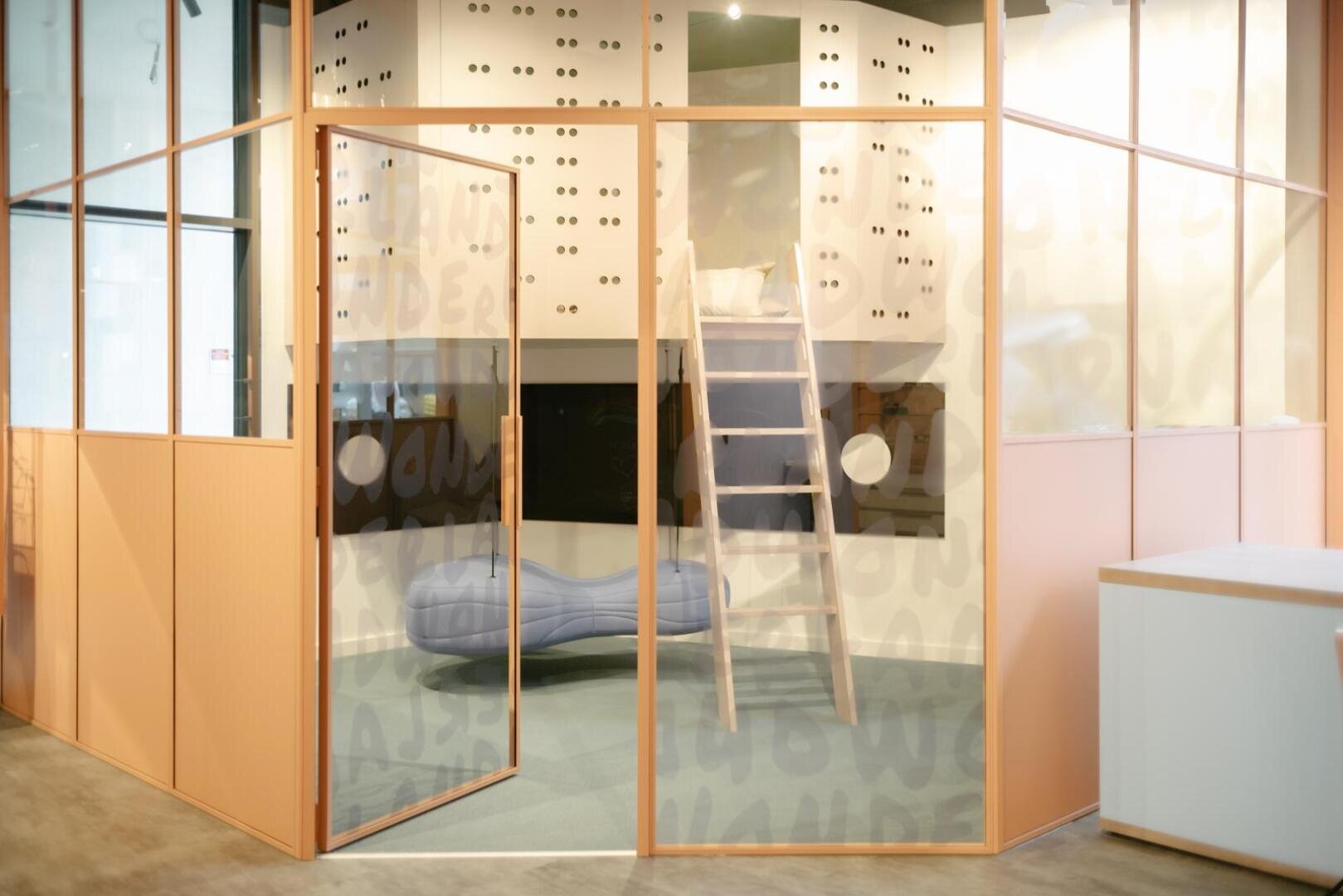 Ein modernes Spielzimmer mit Glaswänden bietet ein kleines weißes Loft mit einer Leiter, einer zartblauen Bank und pastellrosa Rahmen. An der Wand befinden sich verspielte Ausschnitte und das Wort WONDER, das sich im Hintergrund schwach wiederholt.
