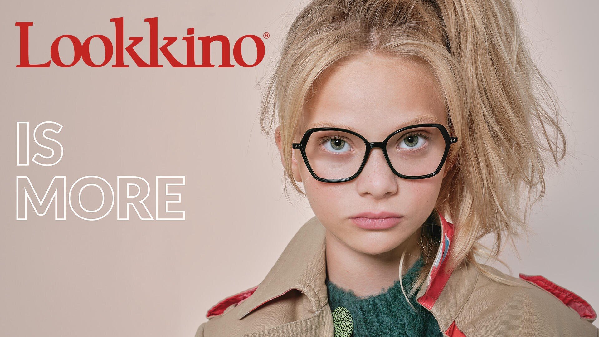 Eine junge Person mit langen blonden Haaren, die zu einem hohen Pferdeschwanz gebunden sind, trägt eine große Brille mit schwarzem Rand und einen hellbraunen Mantel. Auf hellem Hintergrund steht „Lookkino IS MORE“.