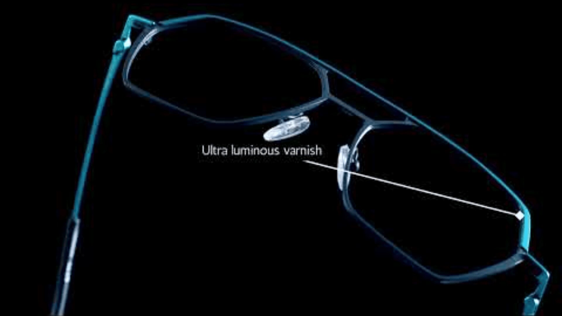 A close-up of eyeglasses with a blue frame on a black background. A label points to the frame, reading Ultra luminous varnish, highlighting the frame’s glossy or luminous coating.