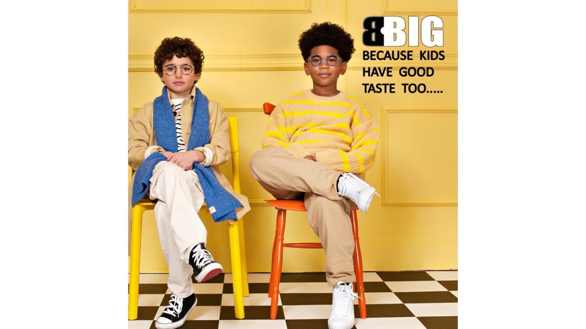 Zwei stylische Kinder sitzen auf gelben und orangefarbenen Stühlen vor einer gelben Wand. Einer trägt eine Brille, eine beige Jacke und weiße Hosen, der andere einen gelben Pullover und Jeans. Text: GROSS, WEIL AUCH KINDER GUTEN GESCHMACK HABEN….