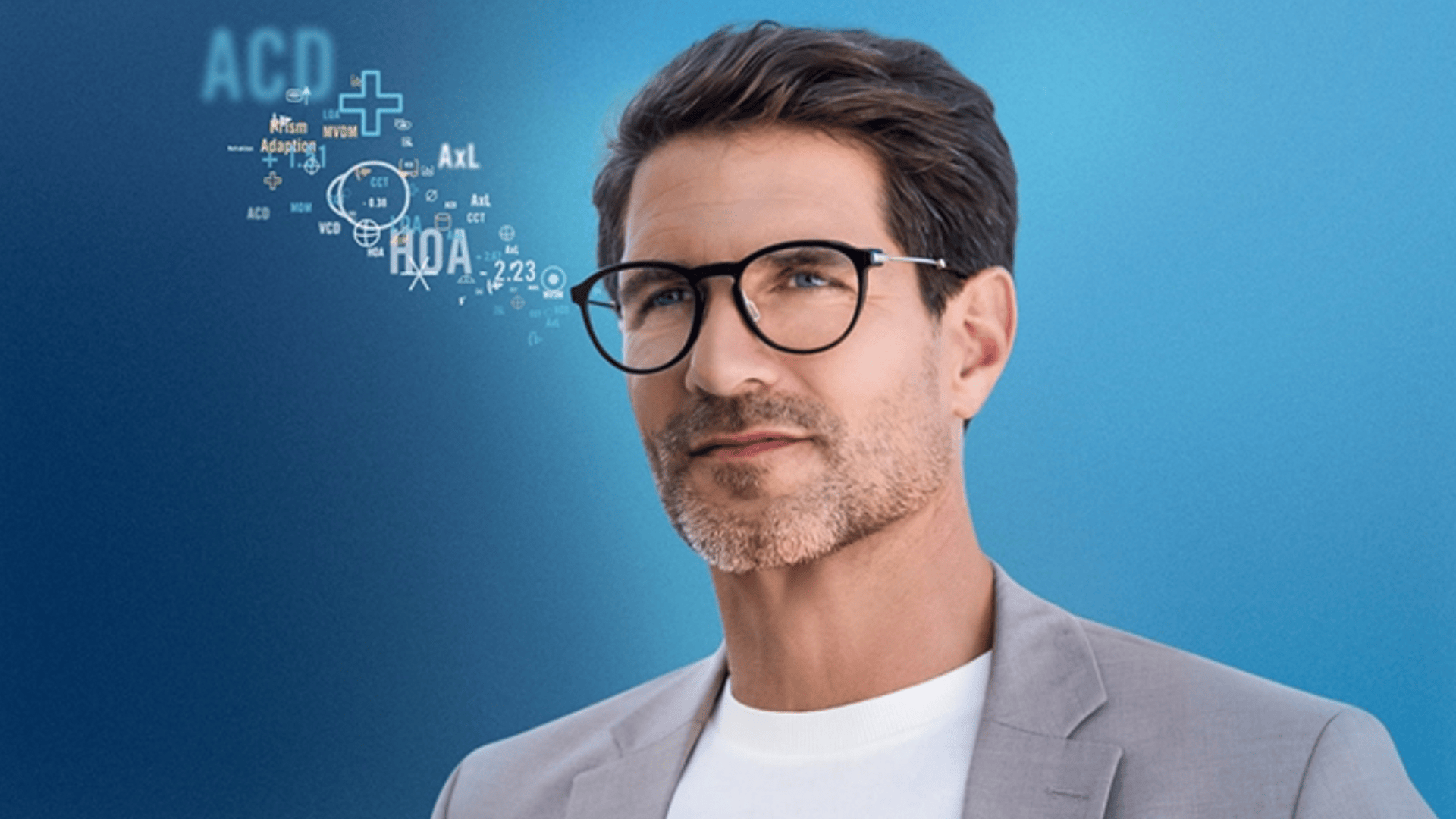 A man with short brown hair, wearing glasses, a light gray blazer, and a white shirt stands in front of a blue background with digital medical symbols and text near his head.