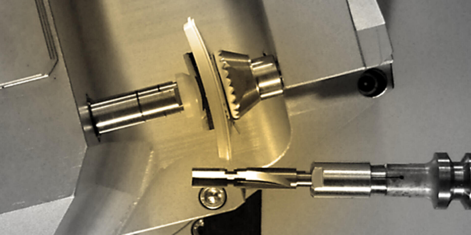 Close-up of a metal gear being precisely cut or machined by two special tools in a manufacturing or construction environment.