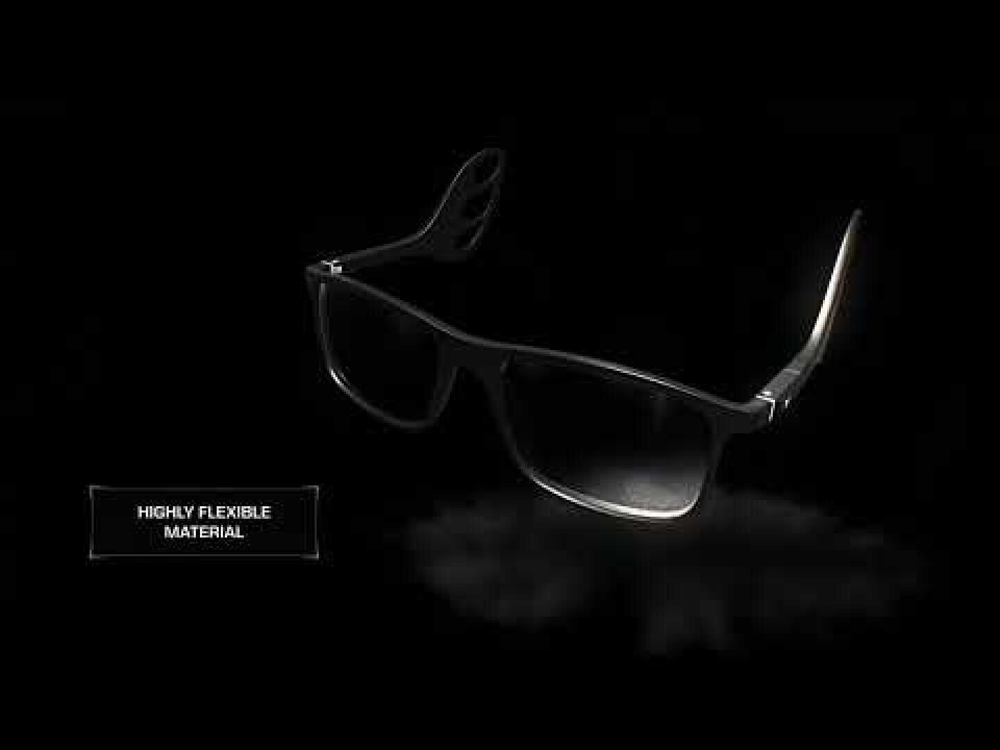 Black glasses with flexible temples are shown on a dark background. A label in the picture says "Highly flexible material".