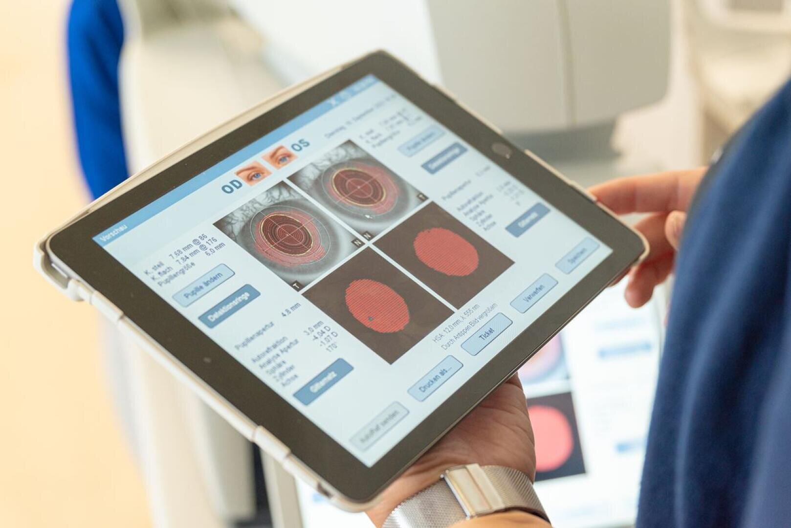 Eine Person hält ein Tablet in der Hand, auf dem die Ergebnisse eines Augenscans mit Bildern der Netzhaut und verschiedenen Diagnosedaten angezeigt werden, wahrscheinlich für eine Augenuntersuchung oder eine Beurteilung des Sehvermögens.